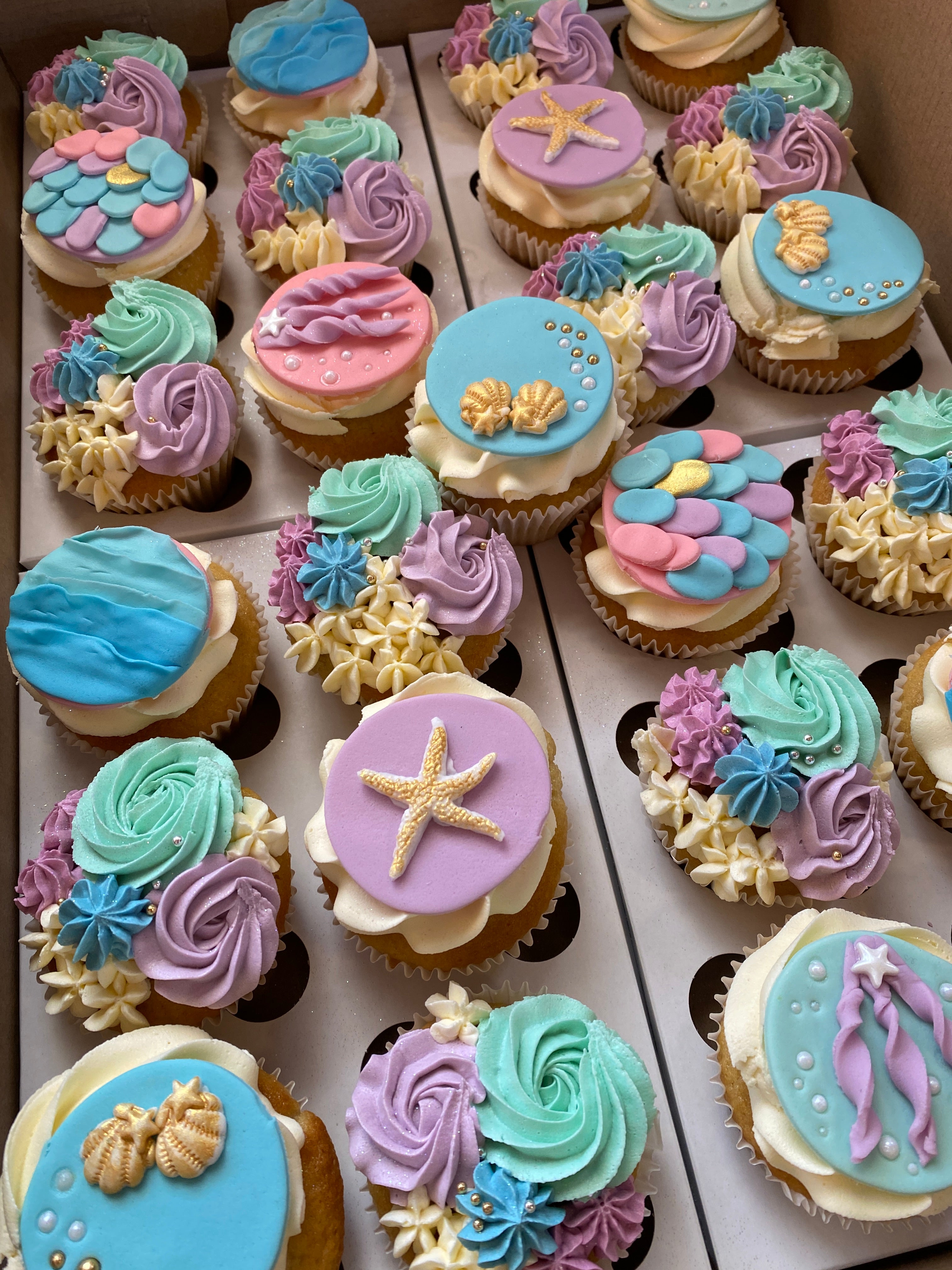 Assorted cupcakes with colorful frosting and decorative elements on a white tray.