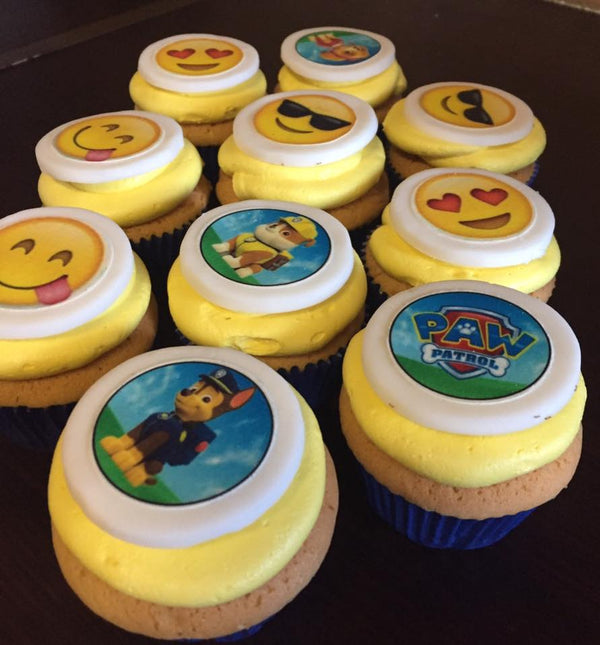 Cupcakes with emoji and Paw Patrol-themed decorations on a dark surface